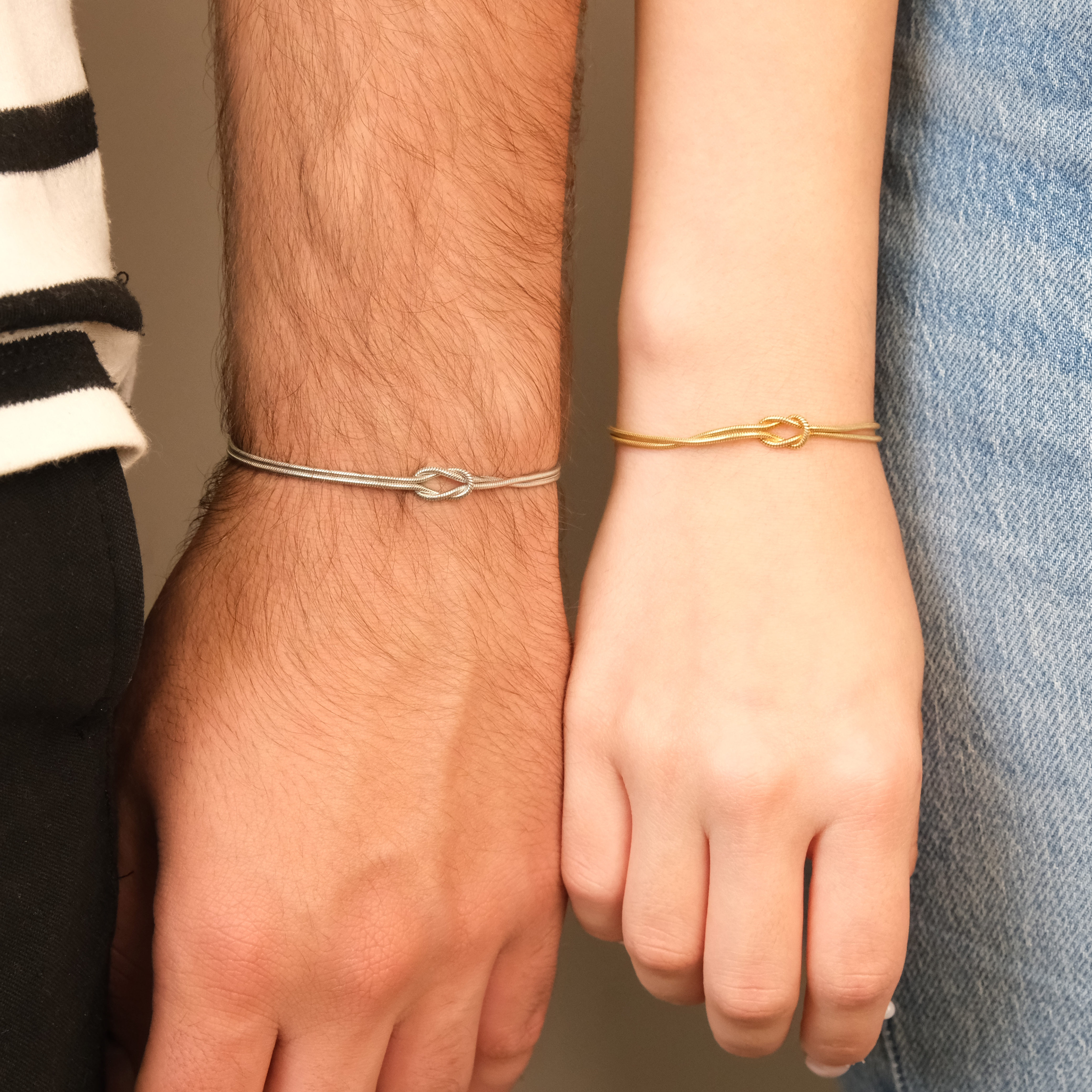 Two wrists wearing silver and gold bracelets against a neutral background