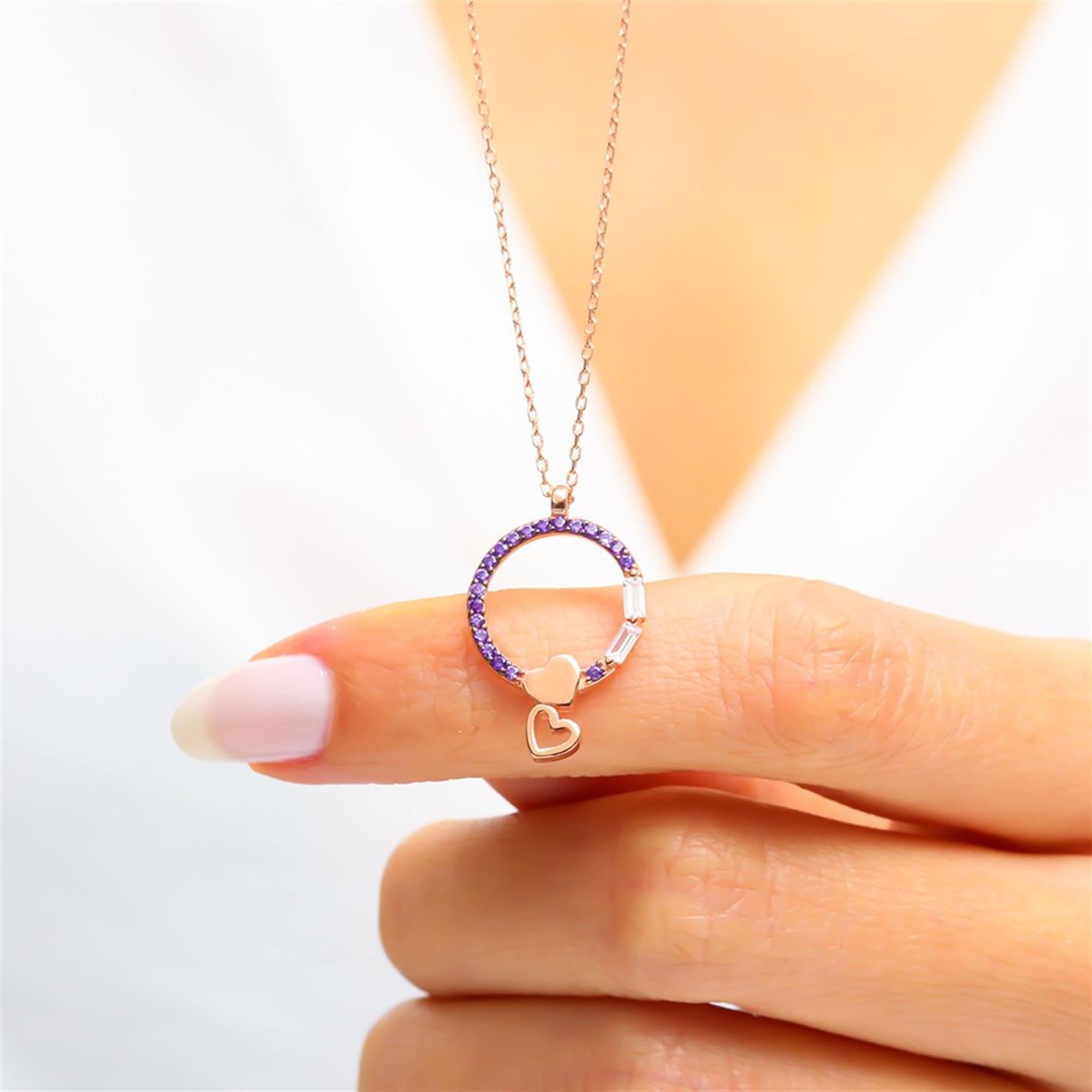 Close-up of a rose gold necklace featuring a circular amethyst setting with baguette-cut stones and two dangling heart charms – a romantic gift for her.