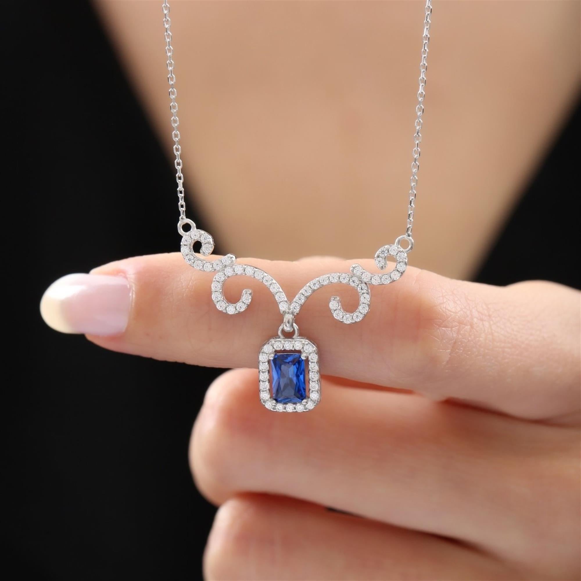 Collar elegante en tono plateado con colgante de circonita azul corte esmeralda inspirado en la realeza y detalles curvos de zirconia – perfecto para un look atemporal
