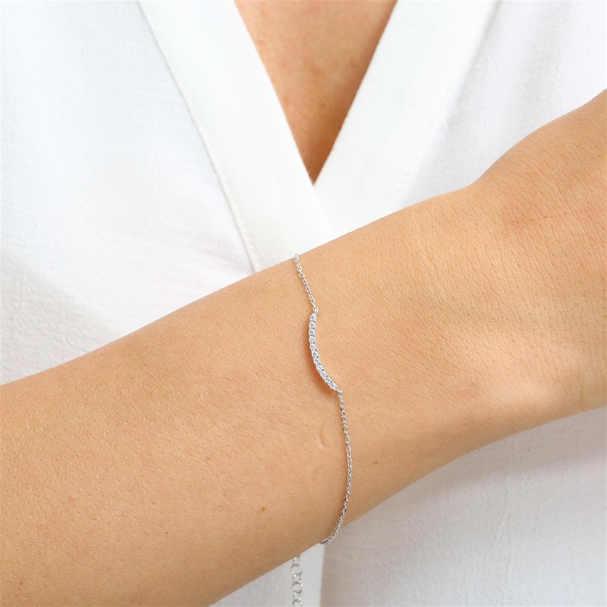 Sleek sterling silver bracelet with a curved wave design and diamond-like zirconia stones, perfect for elegant layering.