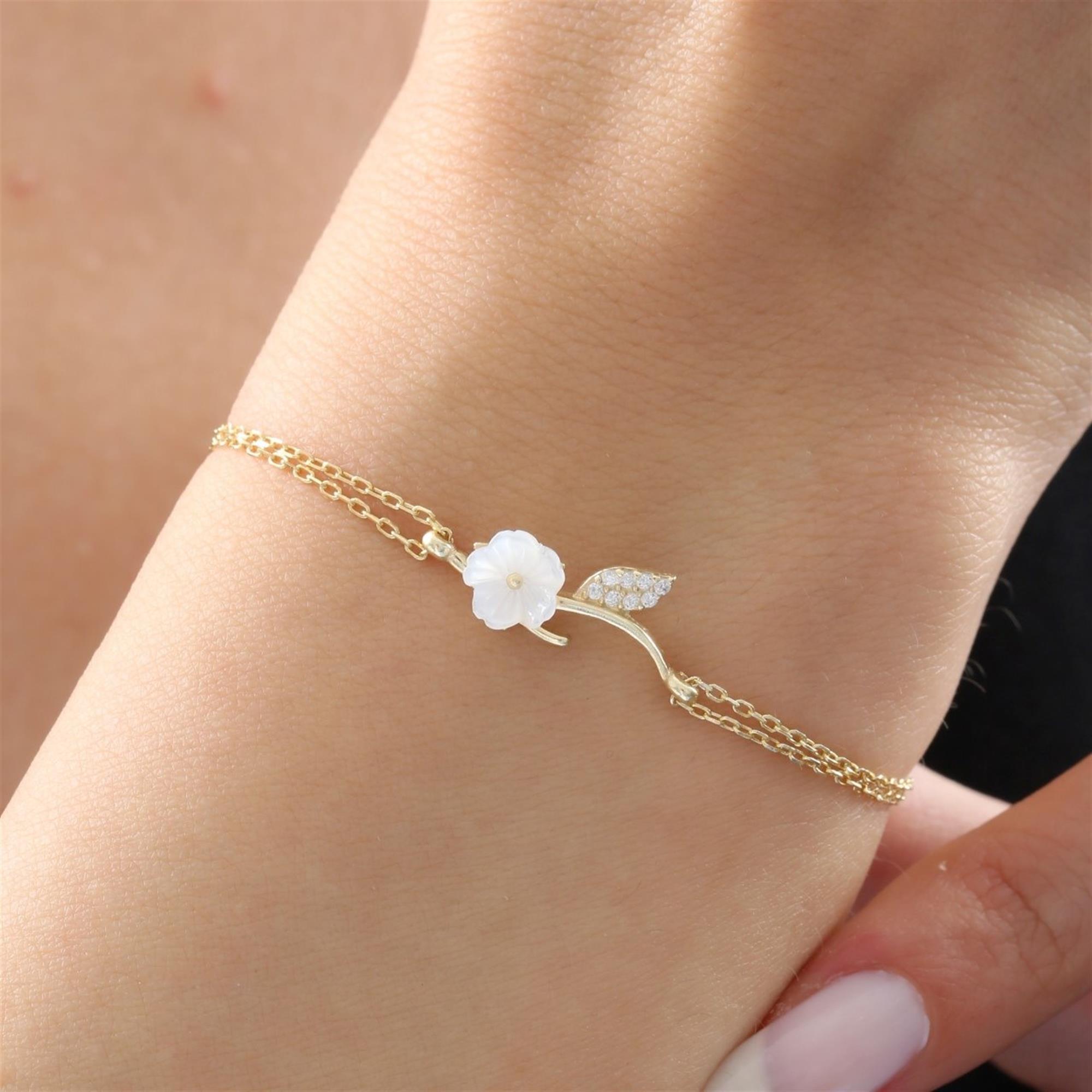 Pulsera dorada con flor blanca tallada y hoja de circonita – diseño inspirado en la naturaleza