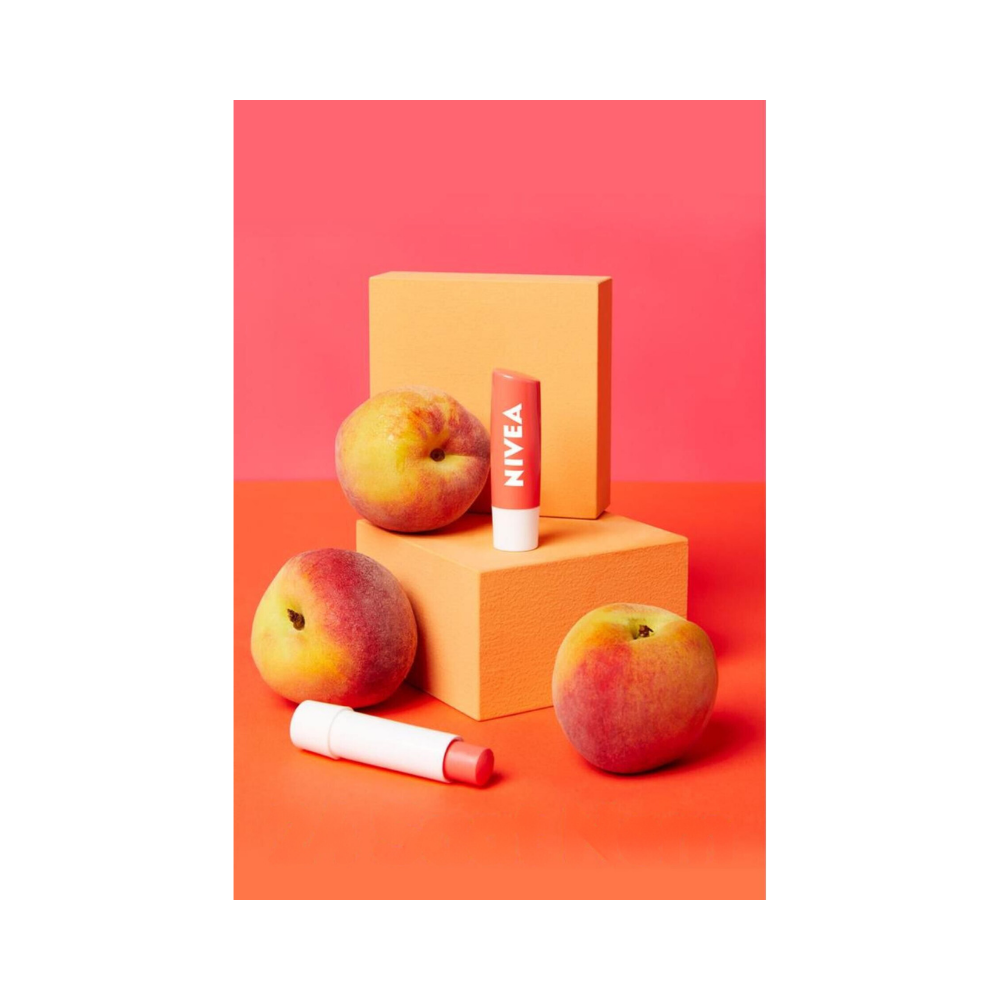 Set of four Nivea lip balms on a white surface, each with a peach-themed label and cap.