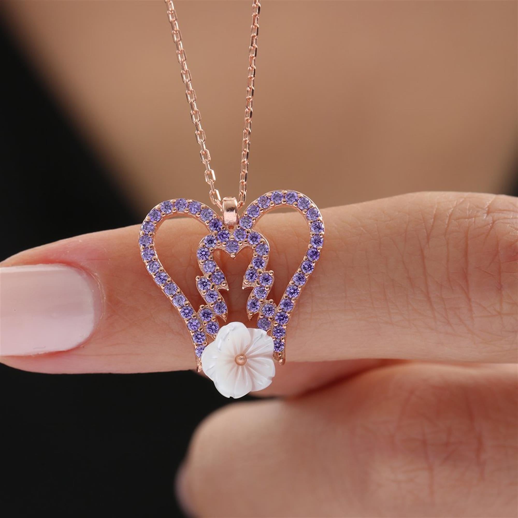 Collar de alas de ángel en oro rosa con circonitas moradas y flor de magnolia tallada – símbolo de amor y serenidad.