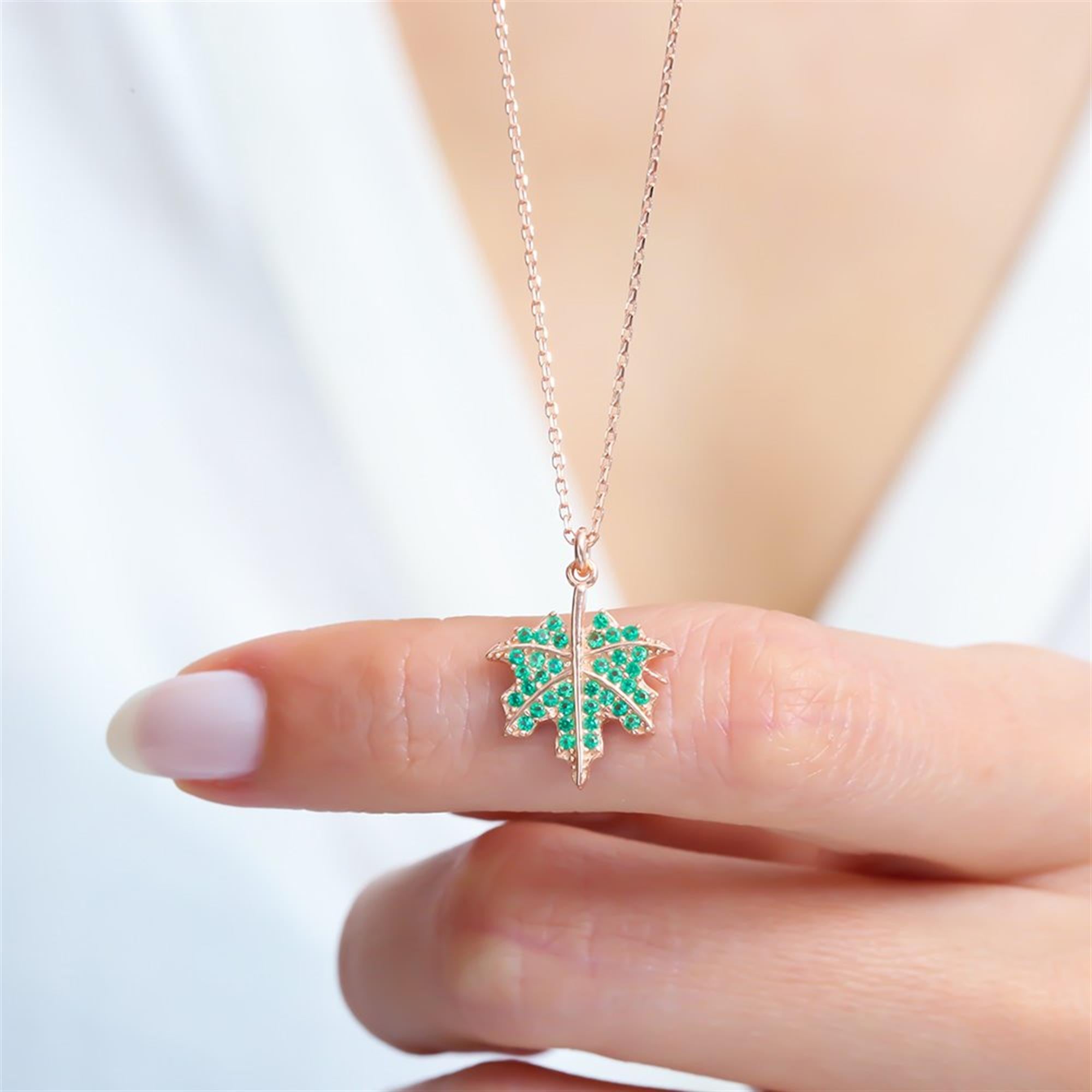Rose gold maple leaf necklace with emerald green cubic zirconia stones – a nature-inspired pendant symbolizing strength and beauty.