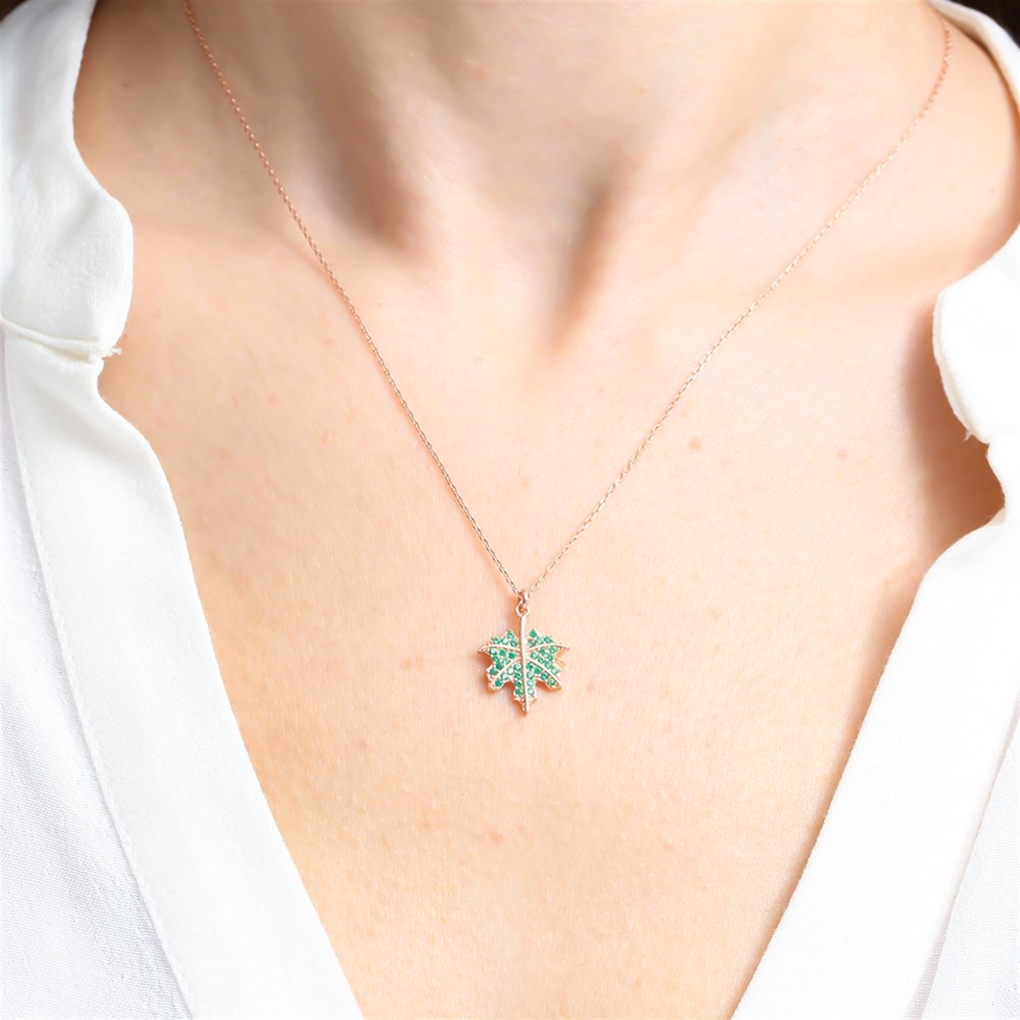Collar de hoja de arce en oro rosa con piedras verdes esmeralda – un colgante inspirado en la naturaleza que simboliza fuerza y belleza.